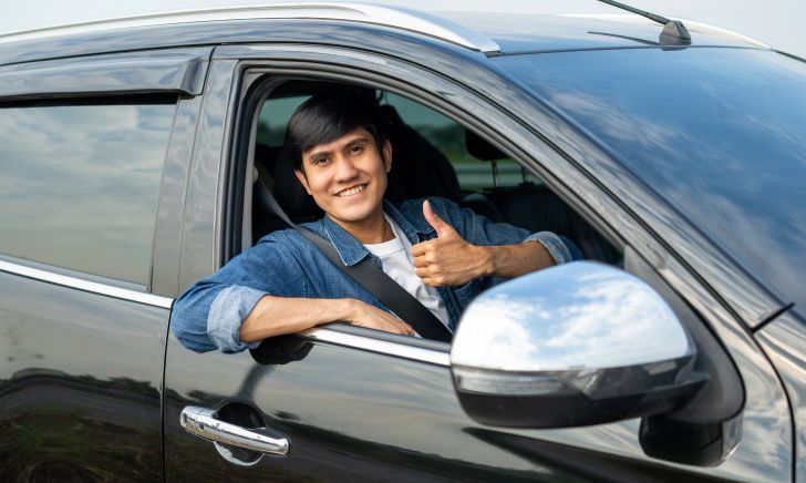 A man sitting in his car gives a thumbs up symbolizing satisfaction with car ownership in Singapore